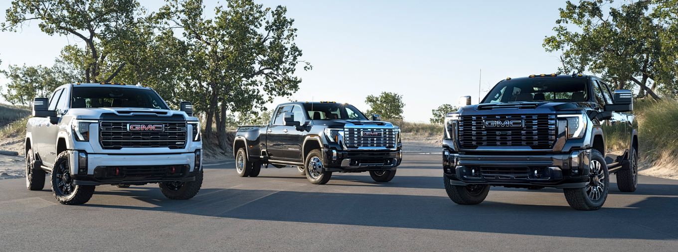Three 2023 GMC Sierra 2500 HD models lined up on a road with trees in the background